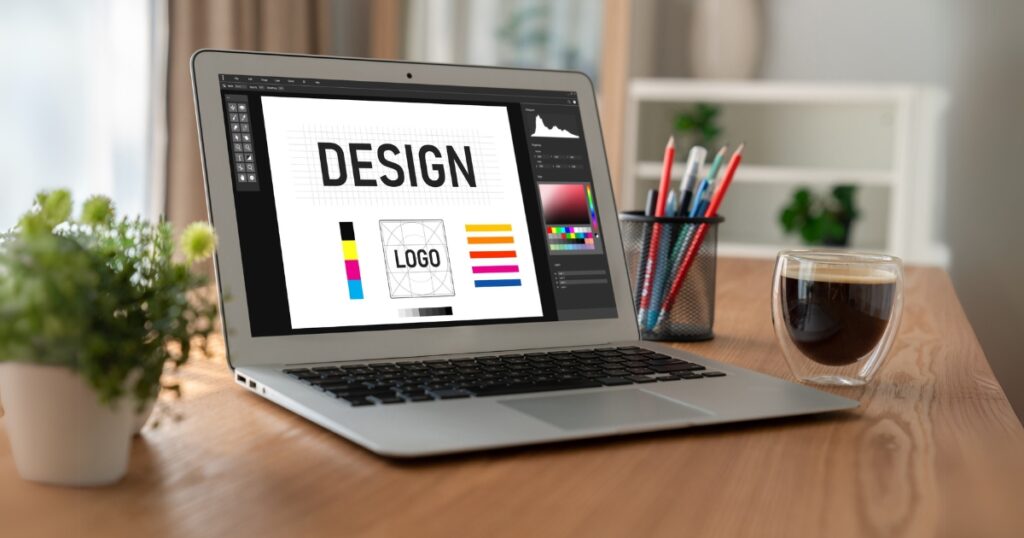 A laptop on a wooden desk displaying a graphic design software interface with the words "DESIGN" and "LOGO," surrounded by color palettes and layout tools.