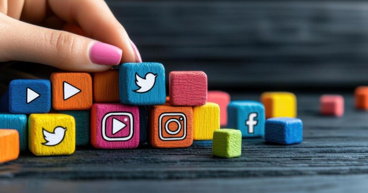 Colorful wooden blocks with social media icons, including Twitter, Instagram, Facebook, and play buttons, arranged on a dark wooden surface with a hand adjusting one of the blocks.